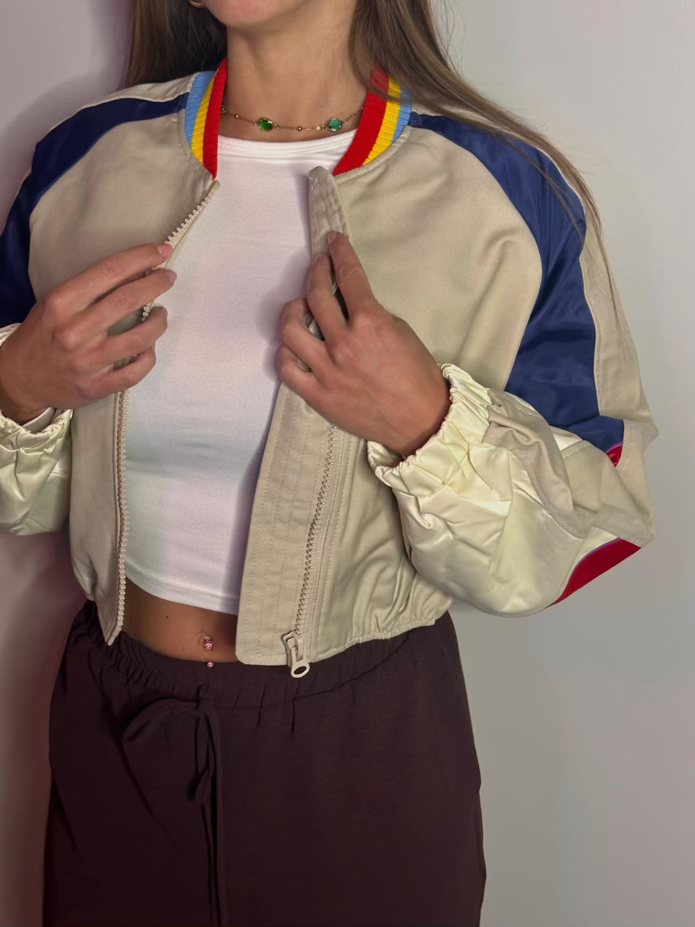 Giacca bomber cropped tricolore indossata su un top bianco e pantaloni marroni. Il modello Retro Groove di Clamont Wear mostra il taglio corto in vita, le maniche a contrasto blu, rosse e crema e il colletto a costine colorate anni '80."