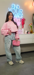 Dettaglio di un outfit composto da jeans baggy chiari modello Starlight con decorazioni brillanti, abbinati a una felpa rosa crop e una borsa fucsia in coordinato.